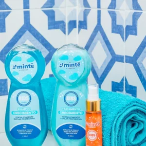 Botellas de shampoo tratamiento y aceite capilar Minte para niños junto a toalla azul sobre fondo de azulejos