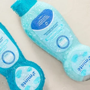 Botellas de shampoo y tratamiento capilar Minte crecimiento color azul con gotas de agua sobre superficie clara