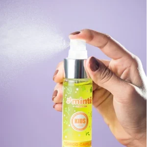 Mano aplicando spray de tónico capilar Minte Kids verde fondo morado