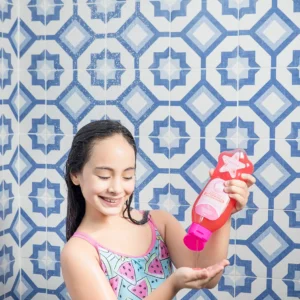 Niña aplicando shampoo para crecimiento Minte Kids en la ducha con fondo de azulejos azules