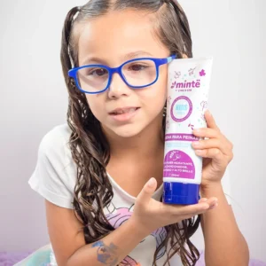 Niña con gafas azules mostrando crema para peinar Minte Kids hidratante y acondicionadora