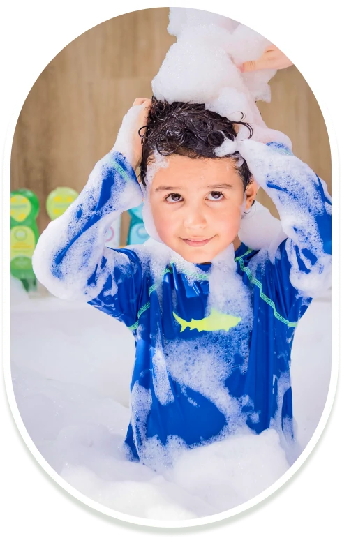 Niño con camiseta azul de tiburón lavando su cabello con espuma de shampoo infantil Minté