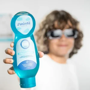 Niño con gafas oscuras sosteniendo botella de shampoo azul Minte crecimiento para niños
