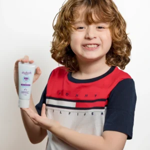 Niño de cabello rizado sonriendo mientras sostiene crema para peinar Minte Kids