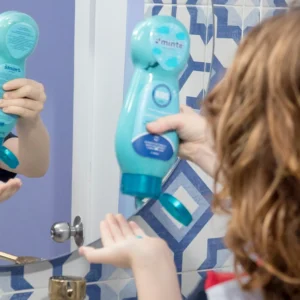 Niño sirviendo tratamiento capilar azul Minte Kids frente al espejo del baño